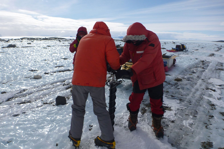 A group of people drilling a hole into a frozen lake